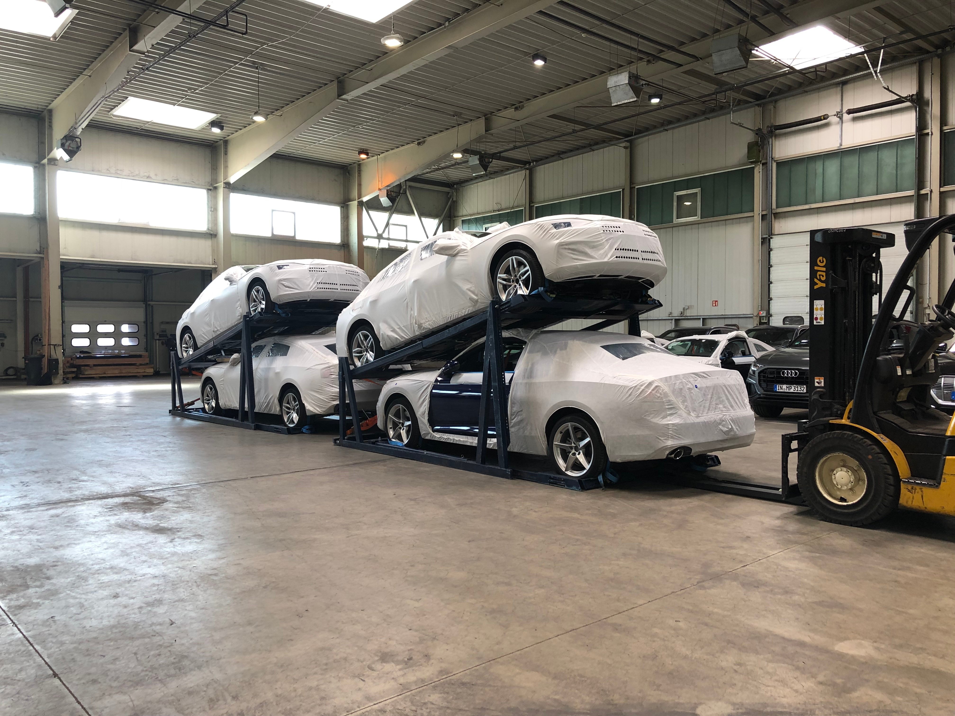 Wrapped new vehicles secured on modular racking inside a warehouse, being prepared for safe containerised transport.