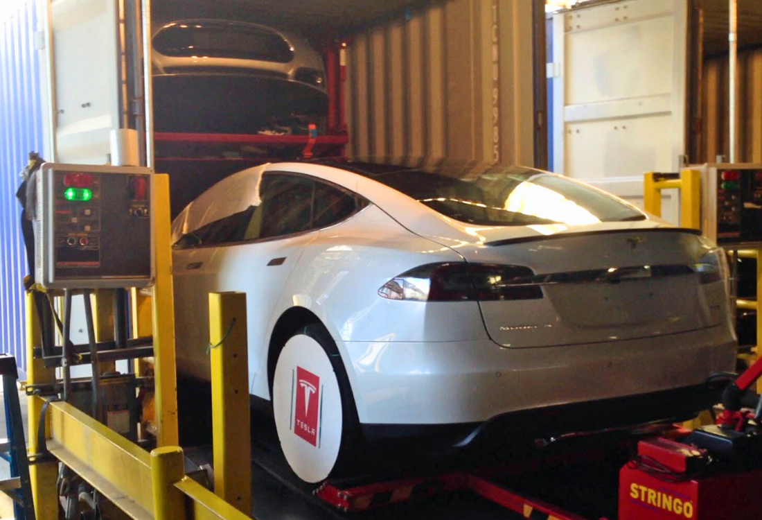 Electric car being loaded into a shipping container on a modular racking system, demonstrating safe and controlled handling for international automotive transport.
