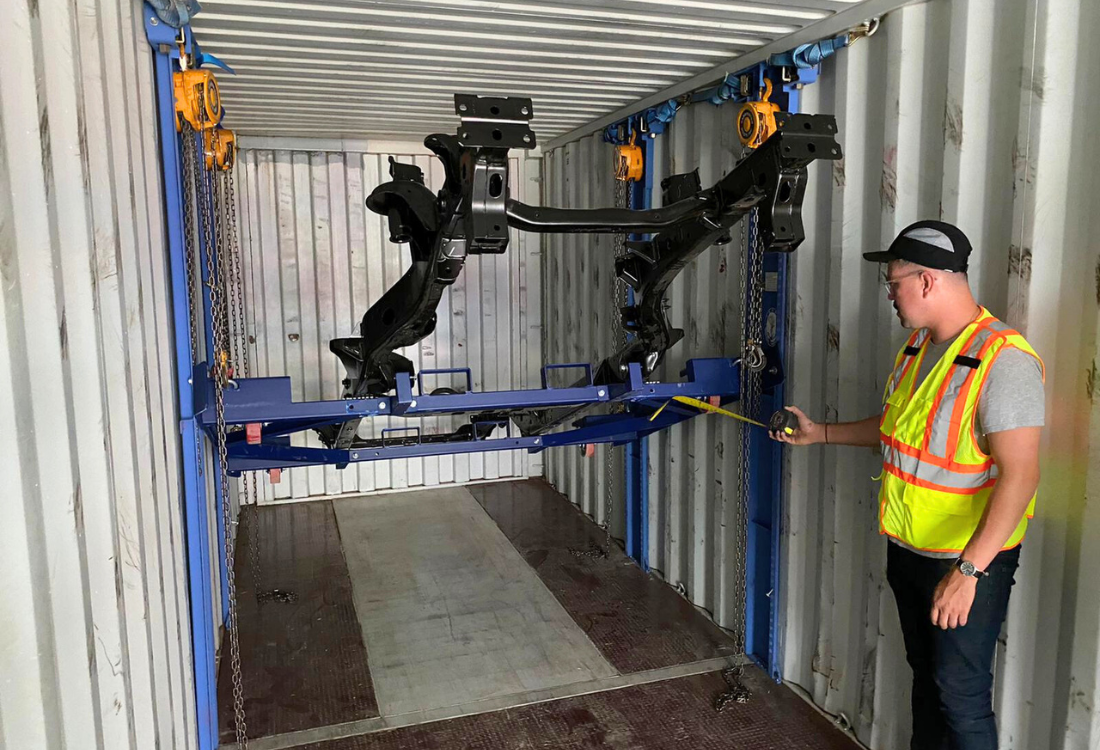 Worker measuring a vehicle chassis secured to a lifting rack inside a shipping container, illustrating how parts and vehicles are safely prepared for international car shipping.