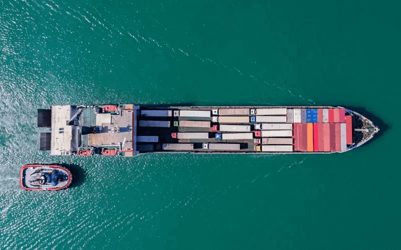 Aerial view of a large cargo ship transporting numerous containers on a clear day, highlighting the complex and potentially hazardous nature of maritime shipping and the safety risks associated with RoRo vessel operations.