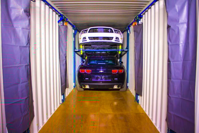 Used cars securely positioned inside a steel shipping container on a raised racking system.