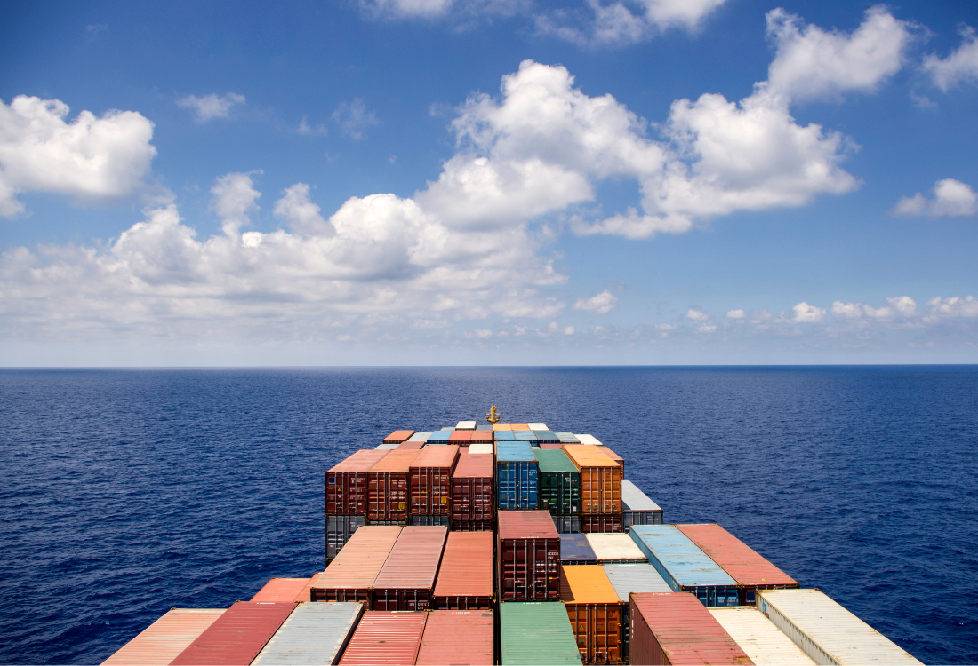A cargo ship carrying stacked multicolored shipping containers moves across the open ocean under a blue sky with scattered clouds, symbolising efficient containerised vehicle transport and space optimisation.