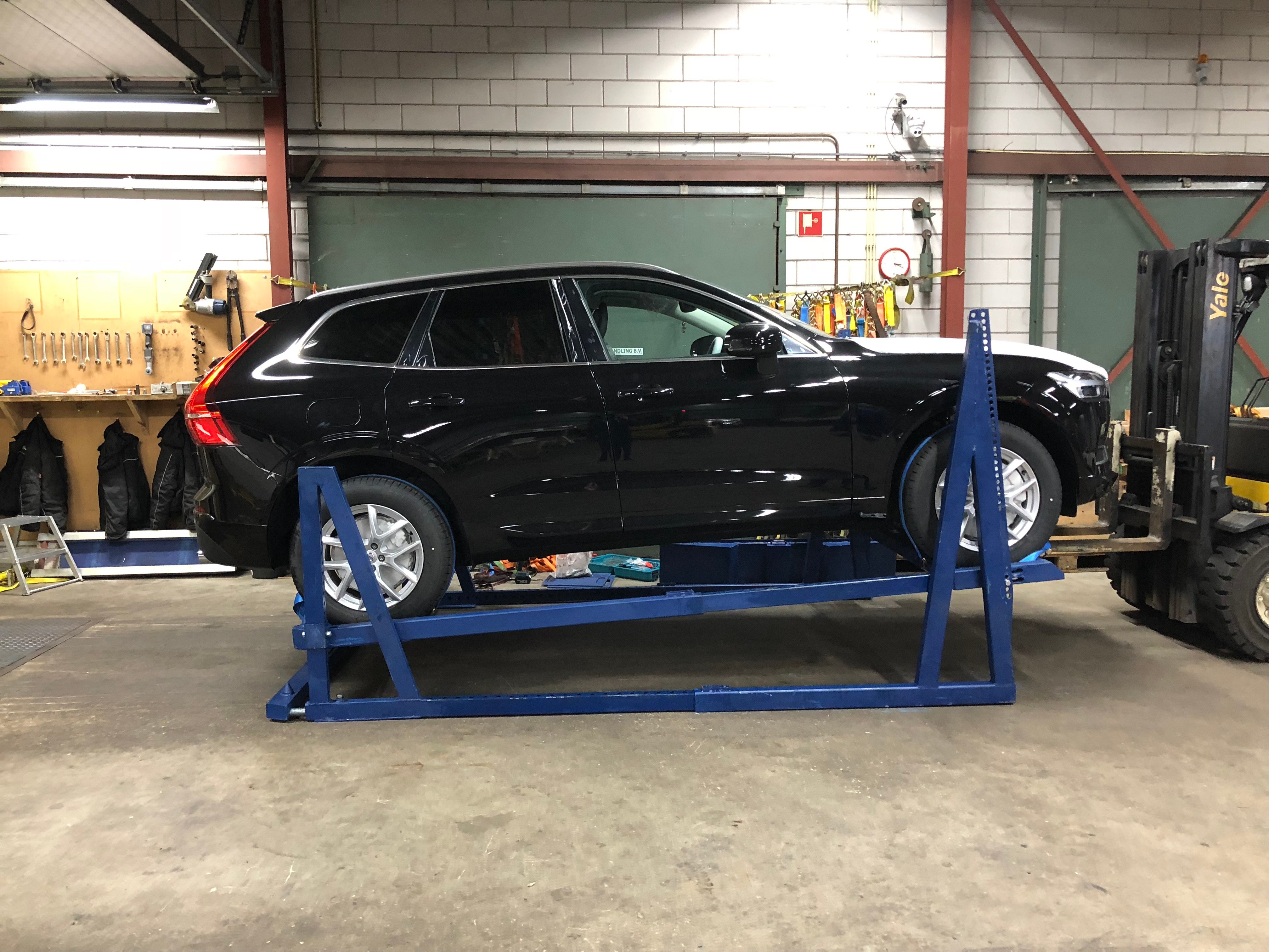 Black Volvo SUV on a blue automotive logistics racking system being prepared for container loading.