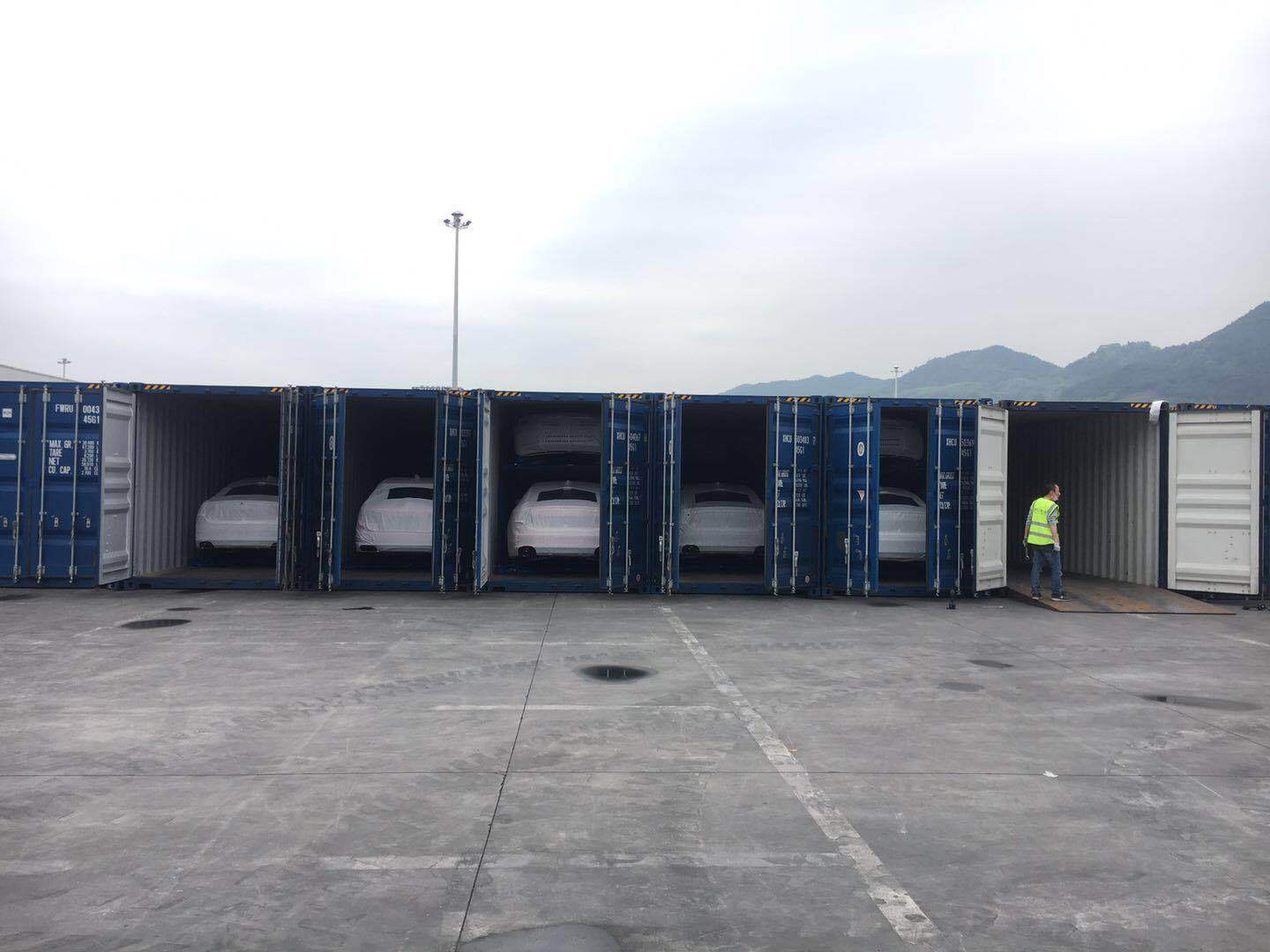 Multiple shipping containers loaded with covered vehicles at a port, prepared for international export as part of automotive logistics operations.