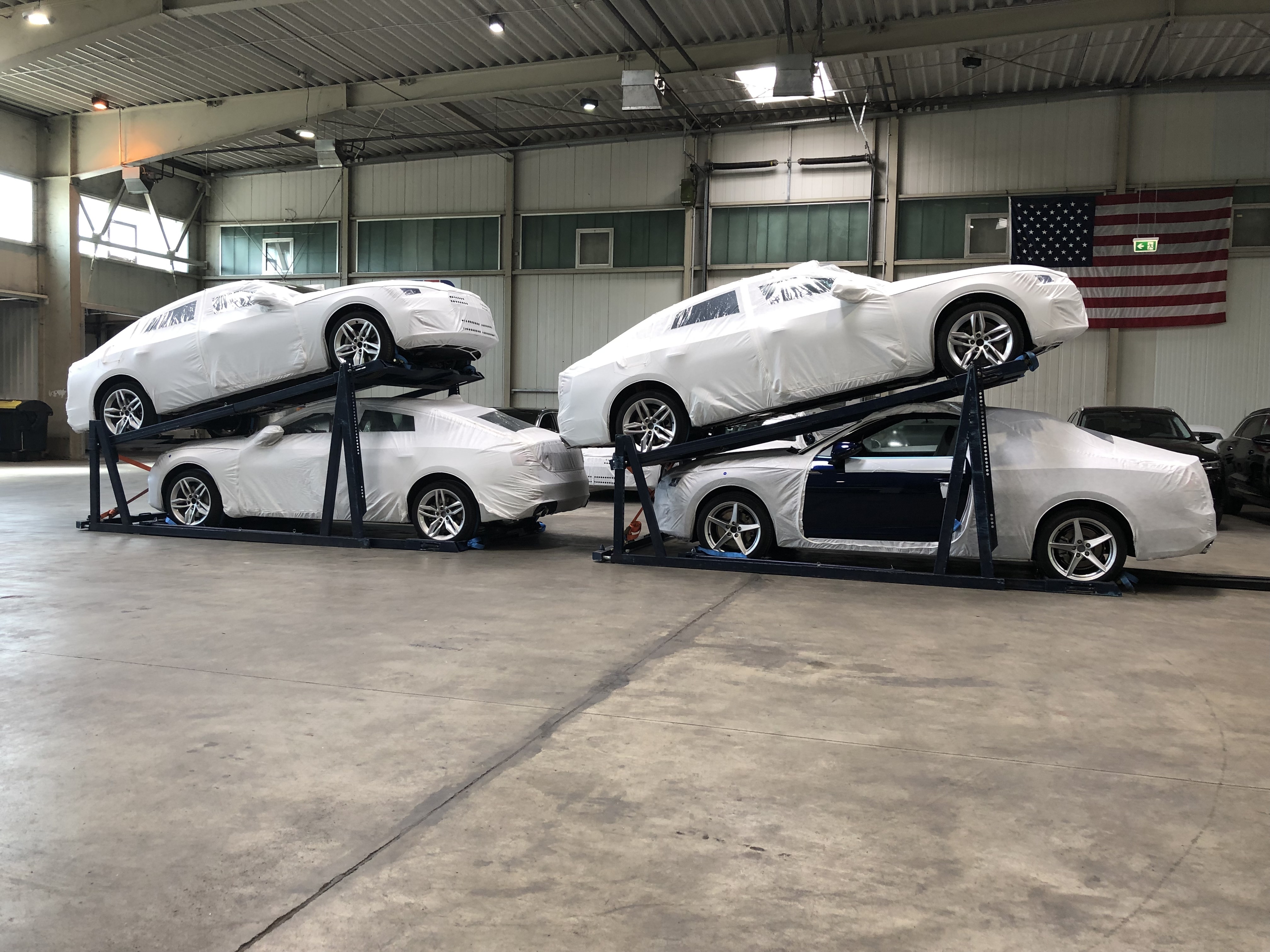 Vehicles positioned on multi-level racking systems for container loading, supporting finished vehicle racking in automotive logistics operations.